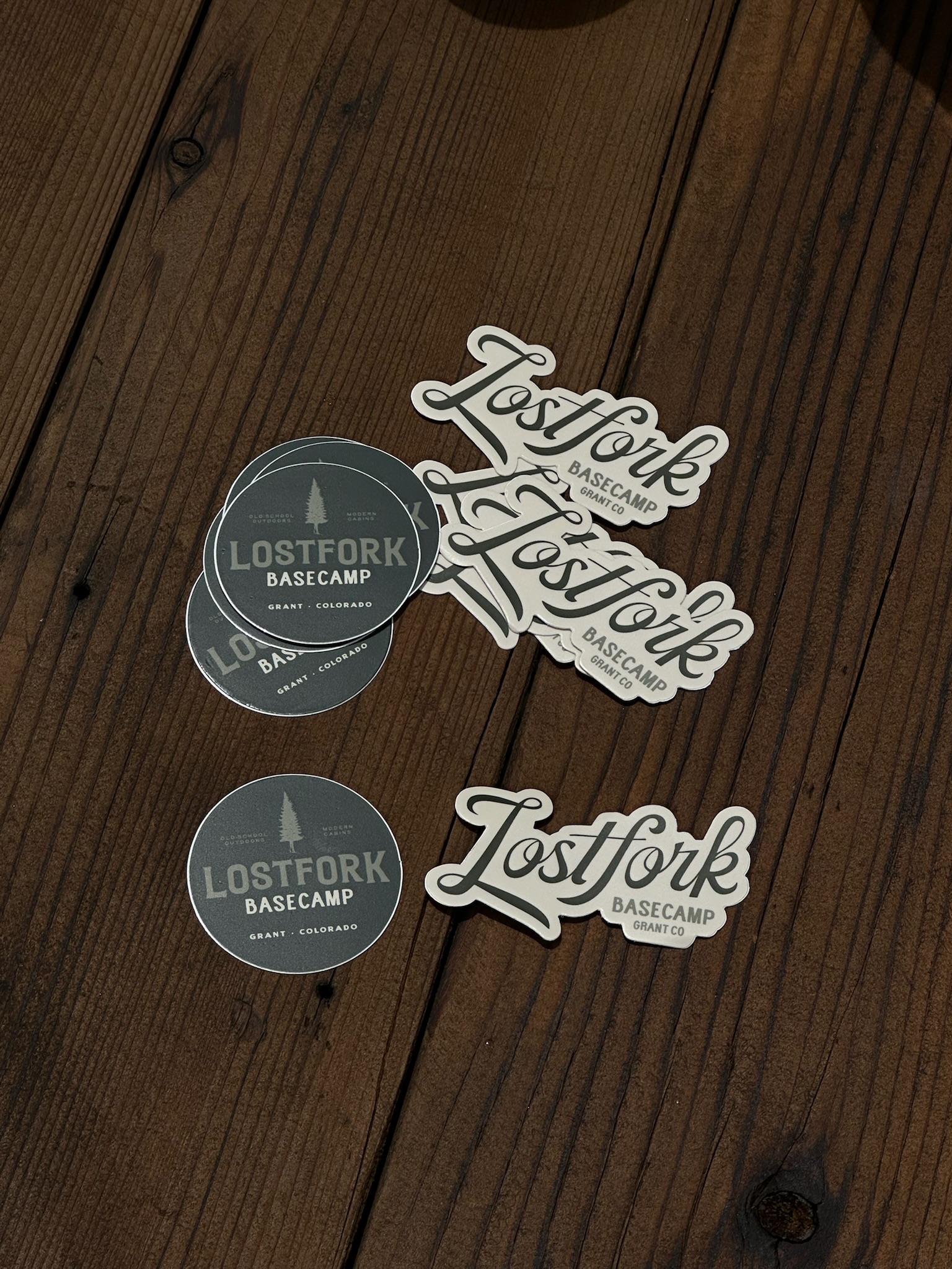 Stickers reading "Lostfork Basecamp Grant, Colorado" are scattered on a wooden surface, including round green stickers and white stickers shaped around the "Lostfork Basecamp" logo.